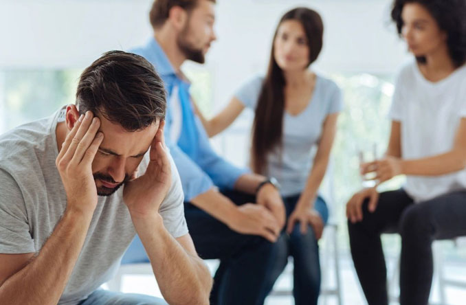 A group of people sitting in a circle with one man holding his head.