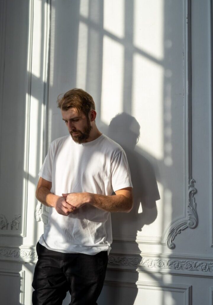 A man standing in front of a wall looking at his watch.